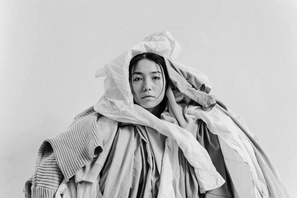 melancholy young asian woman under a pile of neutral colored clothes